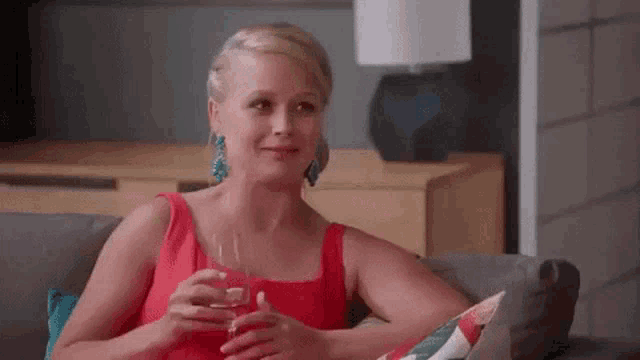 a woman in a red dress is sitting on a couch drinking a glass of wine .