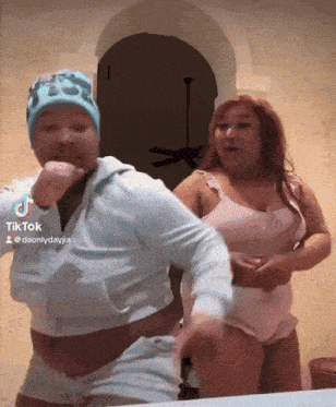two women are dancing in front of a ceiling fan and a sign that says tik tok