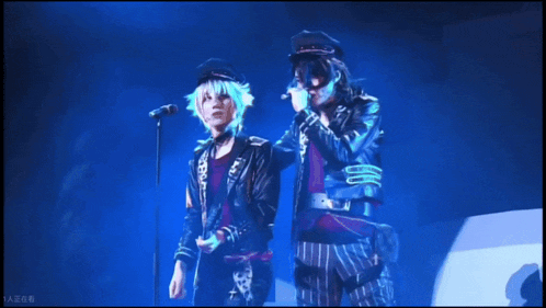 a man singing into a microphone next to another man with a guitar