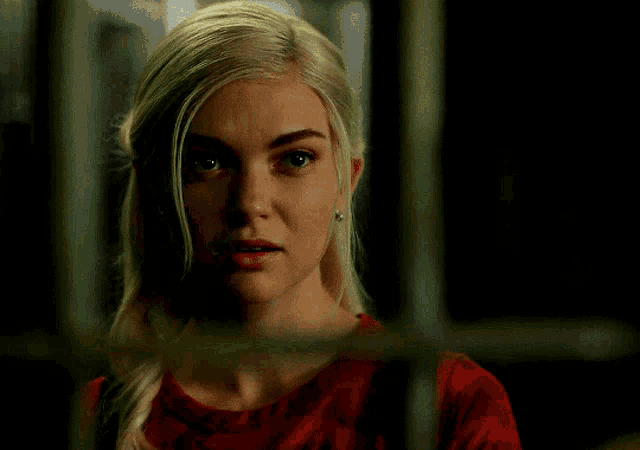 a woman with blonde hair and a red shirt is behind bars
