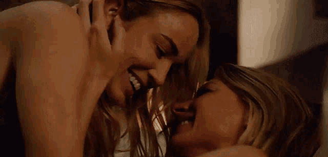 a couple of women are kissing each other and smiling while laying on a bed .