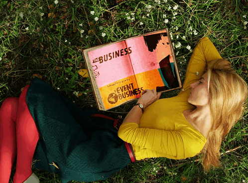 a woman is laying in the grass reading a book titled " event business "