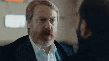 a man with a beard is talking to another man while wearing a suit and tie .