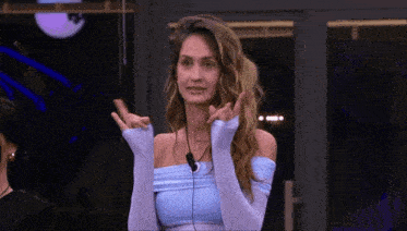 a woman in a blue off the shoulder top and white gloves is giving a peace sign
