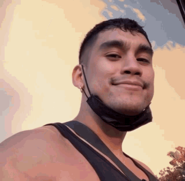 a man wearing a black mask and earrings smiles for the camera