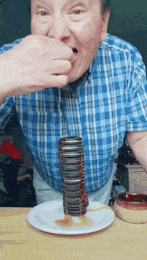 a man in a blue plaid shirt is eating a stack of oreos on a plate .