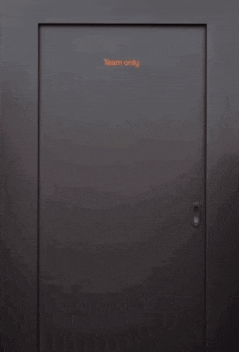 a man in an orange shirt and hat is standing in a doorway holding a bottle of beer .