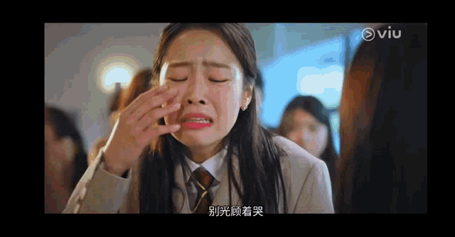 a woman in a suit and tie is crying in front of a group of people in a room .