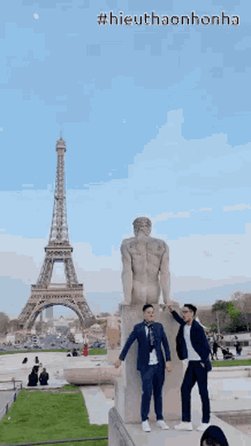 two men standing on a statue in front of the eiffel tower with the caption #hieuthaonhonha