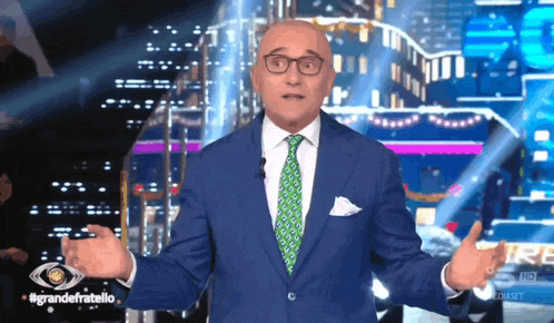 a bald man in a blue suit and green tie stands in front of a large eye
