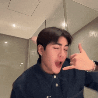a young man in a blue shirt is making a funny face while making a hand gesture .