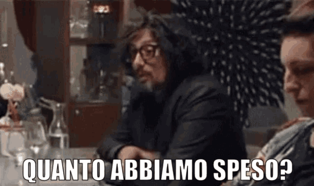 a man with glasses is sitting at a table with a woman and says " quanto abbiamo peso "