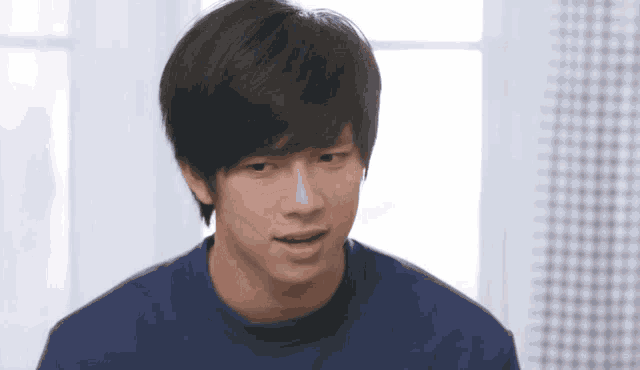 a young man wearing a blue sweater is looking at the camera