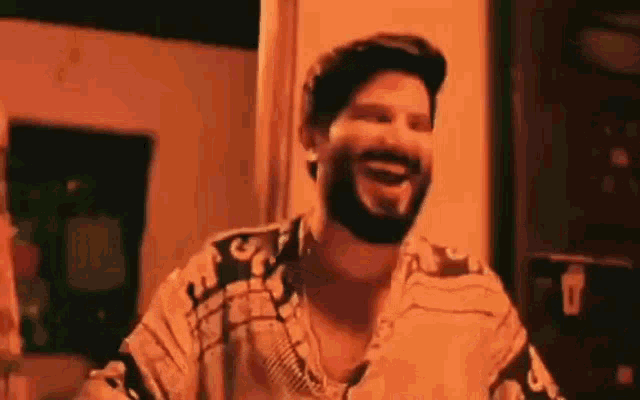 a man with a beard is laughing and smiling in a dark room .