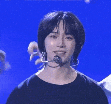 a man with long hair is wearing a microphone and making a heart with his hands .