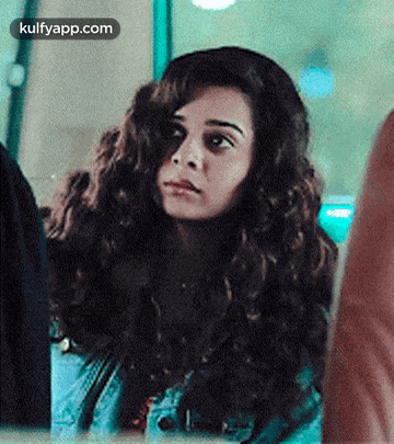 a woman with curly hair is sitting in front of a window and looking out .