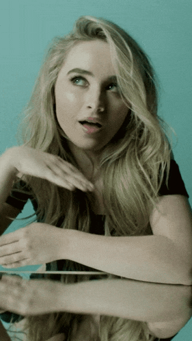 a blonde woman with a surprised look on her face looks at her reflection in a mirror