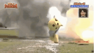 a yellow mascot is standing in the middle of a field with an explosion behind it .