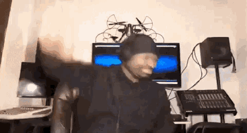 a man wearing headphones and a hat is sitting in front of a computer monitor .