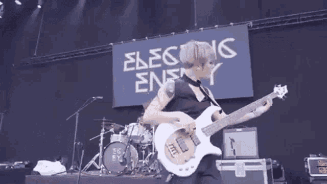 a woman is playing a guitar on stage in front of a sign that says electing enemy .