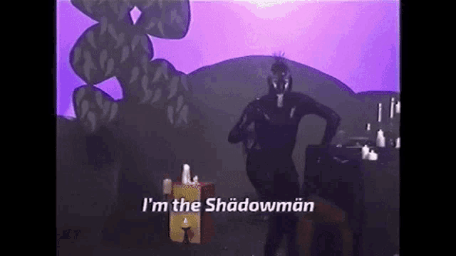 a man in a black suit is dancing in front of a purple background and says i 'm the shadowman .