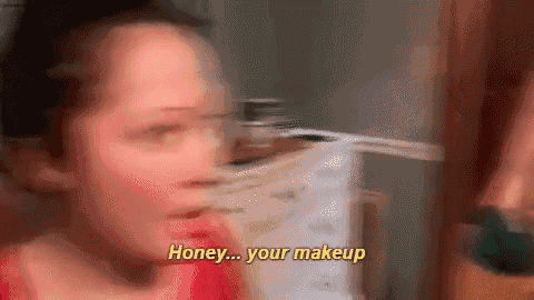 a woman is talking to another woman in front of a mirror while applying makeup .