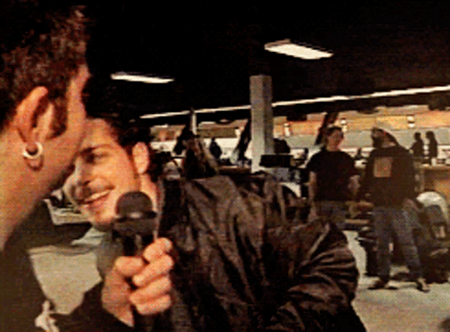 a man holding a microphone talks to another man in a dark room
