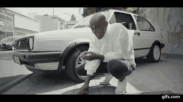a man is squatting in front of a white car with a ford logo on it