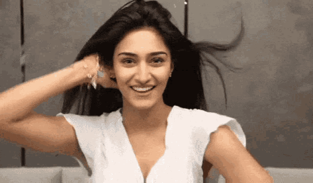 a woman wearing a white shirt is smiling and holding her hair