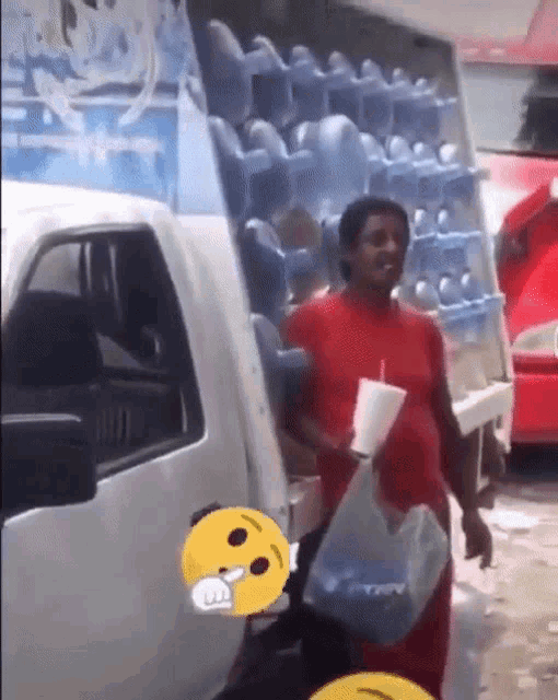 a man in a red shirt is carrying a cup and a bag of water