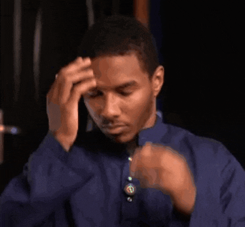 a man in a blue shirt is holding his head in his hands .
