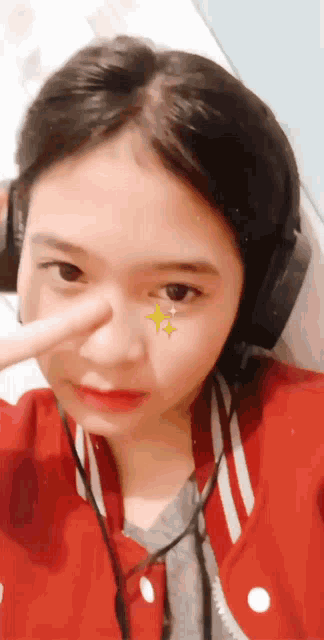 a girl wearing headphones and a red jacket has a star on her face
