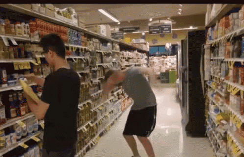 two men are shopping in a grocery store and one of them is looking at a box of cereal
