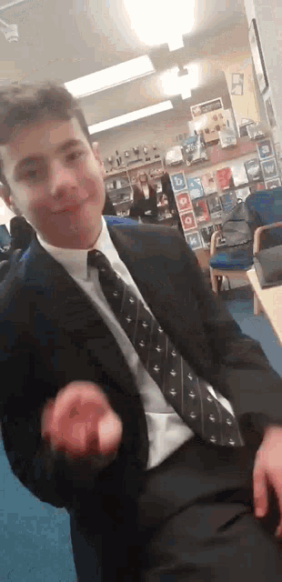 a young man in a suit and tie is sitting at a table in a room .