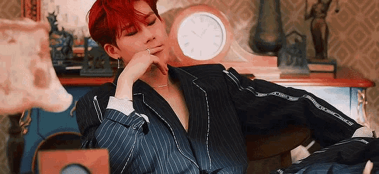 a young man with red hair is sitting in front of a clock