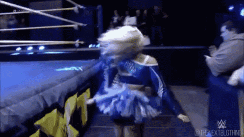 a female wrestler in a blue and white outfit is walking on a wrestling ring .