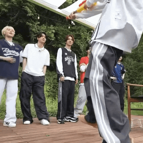 a group of young men are standing on a wooden deck and one of them is holding a water gun .