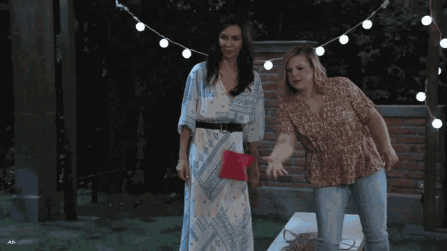 two women standing next to each other with one holding a red pillow in her hand