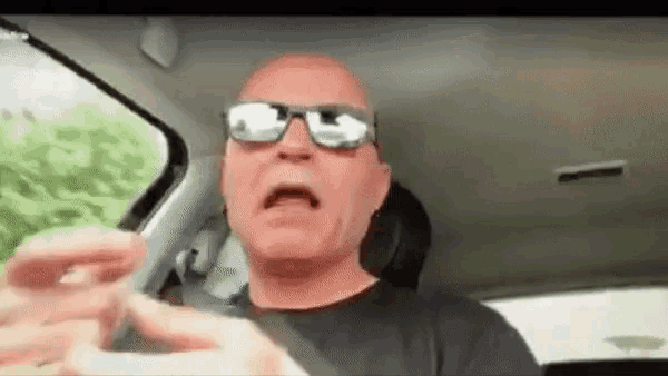 a bald man wearing sunglasses is sitting in a car and making a funny face .