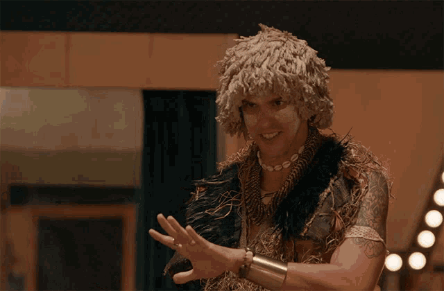 a man wearing a wig and feathers is smiling and making a gesture