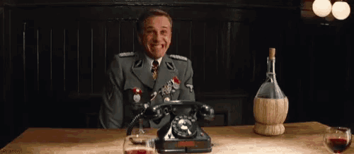 a man in a military uniform is sitting at a table with a phone and a bottle of wine