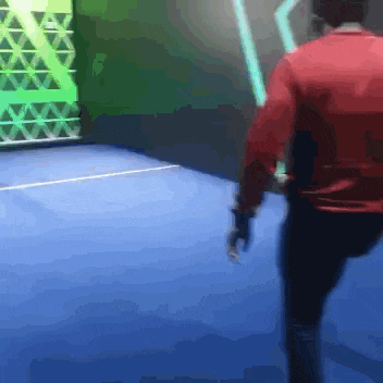 a man in a red jacket is walking on a blue floor