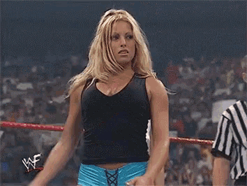 a woman is standing in a wrestling ring wearing shorts and a tank top .