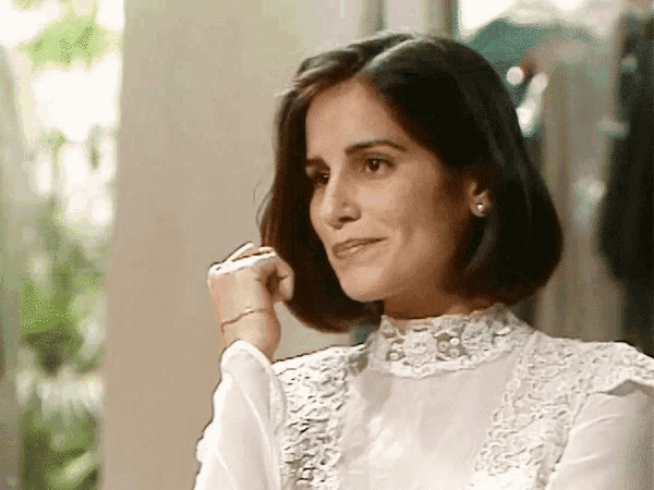a woman wearing a white lace top is smiling and touching her hair