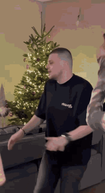a man in a black shirt is dancing in front of a christmas tree in a living room .