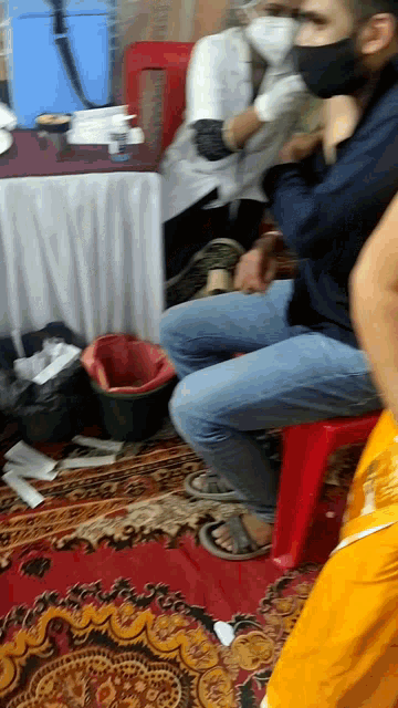 a man wearing a black mask sits on a red stool