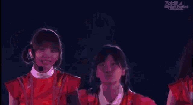 a group of young women are standing next to each other on a stage and one of them is wearing a red dress .