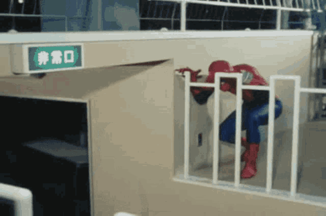 a man in a spiderman costume climbs a fence next to a green exit sign