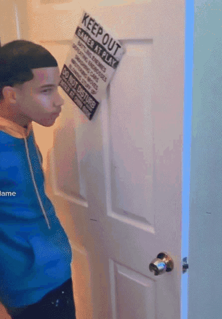 a young boy stands in front of a door with a keep out sign on it