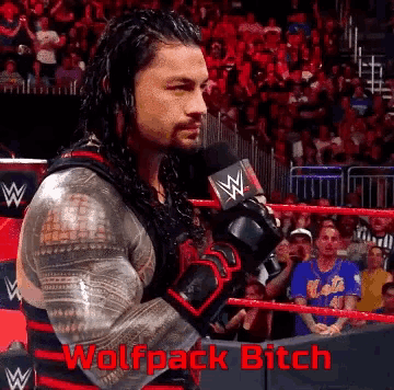 a man in a wrestling ring talking into a microphone with the words wolfpack bitch in red